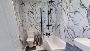 Ein Badezimmer mit Toilette, Badewanne und Waschbecken, alles mit marmorähnlichen Wandfliesen.
