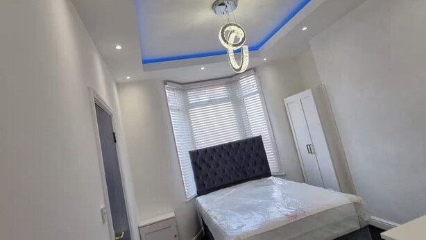 Ein Schlafzimmer mit einem Bett, einem Fenster mit Jalousien, einer Tür und einer Deckenleuchte.