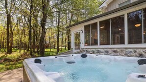 A hot tub in a wooded area with a stone wall and large windows. - Large Poconos Group Retreat with Hot Tub and Game Room (Albrightsville)