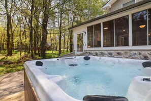 A hot tub in a wooded area with a stone wall and large windows. - Large Poconos Group Retreat with Hot Tub and Game Room (Albrightsville)