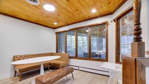 A room with a wooden ceiling, a large window, a brown leather sofa, a white round table, and a bench. - Large Poconos Group Retreat with Hot Tub and Game Room (Albrightsville)