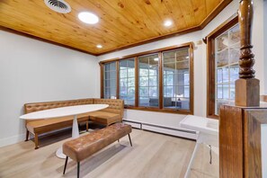 A room with a wooden ceiling, a large window, a brown leather sofa, a white round table, and a bench. - Large Poconos Group Retreat with Hot Tub and Game Room (Albrightsville)