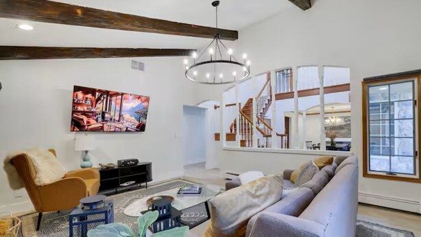 A living room with a large flat-screen TV, a sofa, a coffee table, and a staircase leading to an upper level. - Large Poconos Group Retreat with Hot Tub and Game Room (Albrightsville)