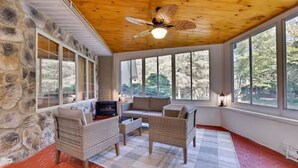 A cozy room with stone walls, large windows, wicker furniture, and a ceiling fan. - Large Poconos Group Retreat with Hot Tub and Game Room (Albrightsville)