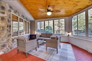 A cozy room with stone walls, large windows, wicker furniture, and a ceiling fan. - Large Poconos Group Retreat with Hot Tub and Game Room (Albrightsville)
