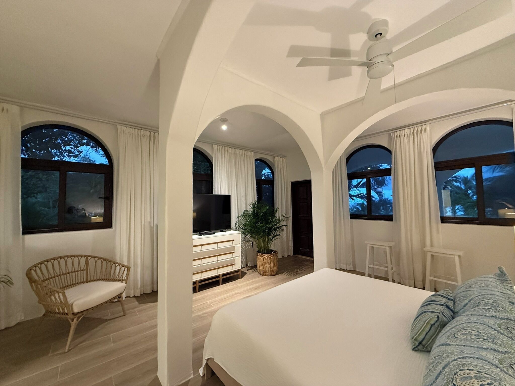 A bedroom with a bed, a television, a chair, and a potted plant.