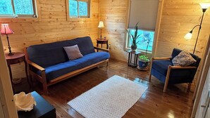 Un interior acogedor de cabaña con piso de madera, un sofá azul, una alfombra pequeña y una planta en maceta.