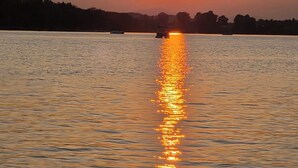 Un atardecer sobre aguas tranquilas, con la silueta de árboles y un barco a lo lejos.