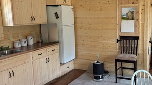 Cocina de cabaña de madera con armarios de madera, un refrigerador, un lavamanos, una silla y un calendario en la pared.