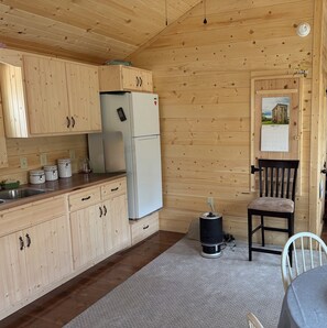 Eine Holzhütte mit einer Küche, inklusive Kühlschrank, Schränken, Spüle und einem Stuhl.