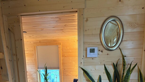 Un interior de madera con una puerta que da a una habitación, un espejo en la pared y un calentador sobre una mesa.