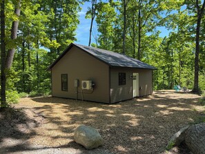 Eine kleine Holzhütte mit einem Metall-Dach, einer Tür und einer Klimaanlage an der Seite.