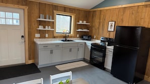Une cuisine de taille réduite avec un revêtement mural en bois, un réfrigérateur noir, un four à micro-ondes et un évier.