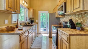 A kitchen with wooden cabinets, a microwave, a refrigerator, and a countertop with a plant. - Pine and Peak – Hot Tub, Fire Pit, Dog Friendly (Gatlinburg)