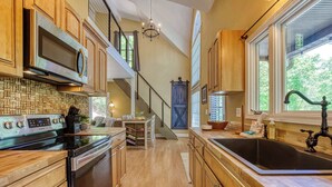 A kitchen with wooden cabinets, a stainless steel range, a black sink, and a staircase leading to another level. - Pine and Peak – Hot Tub, Fire Pit, Dog Friendly (Gatlinburg)