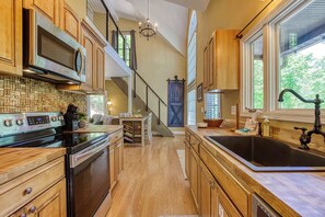 A kitchen with wooden cabinets, a stainless steel range, a black sink, and a staircase leading to another level. - Pine and Peak – Hot Tub, Fire Pit, Dog Friendly (Gatlinburg)