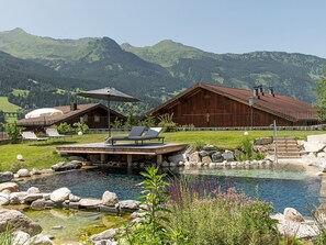 A pool area with lounge chairs, a wooden building, and a mountain backdrop. - 2A Morgensonne/mit Weitblick by Interhome (Bad Hofgastein)