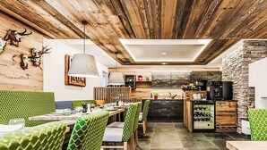 A modern kitchen with wooden beams, a dining area with green upholstered chairs, and a stone accent wall. - 2A Morgensonne/mit Weitblick by Interhome (Bad Hofgastein)