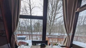 A room with a large window, a laptop on a woven mat, a small plant, and a view of a snowy deck outside. - Troll Hill Nordic Nature Retreat (Municipality Of Chatham-Kent)