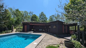 A swimming pool with a stone deck, a wooden structure with seating, and surrounding greenery. - Troll Hill Nordic Nature Retreat (Municipality Of Chatham-Kent)
