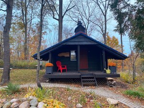 A small wooden cabin with a porch, a red chair, and a welcome sign.