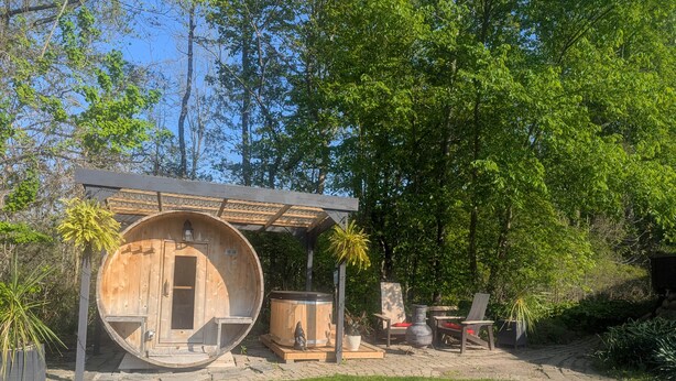 A rustic outdoor structure with a wooden barrel-shaped room, a covered seating area, and a stone pathway leading to it. - Troll Hill Nordic Nature Retreat (Municipality Of Chatham-Kent)