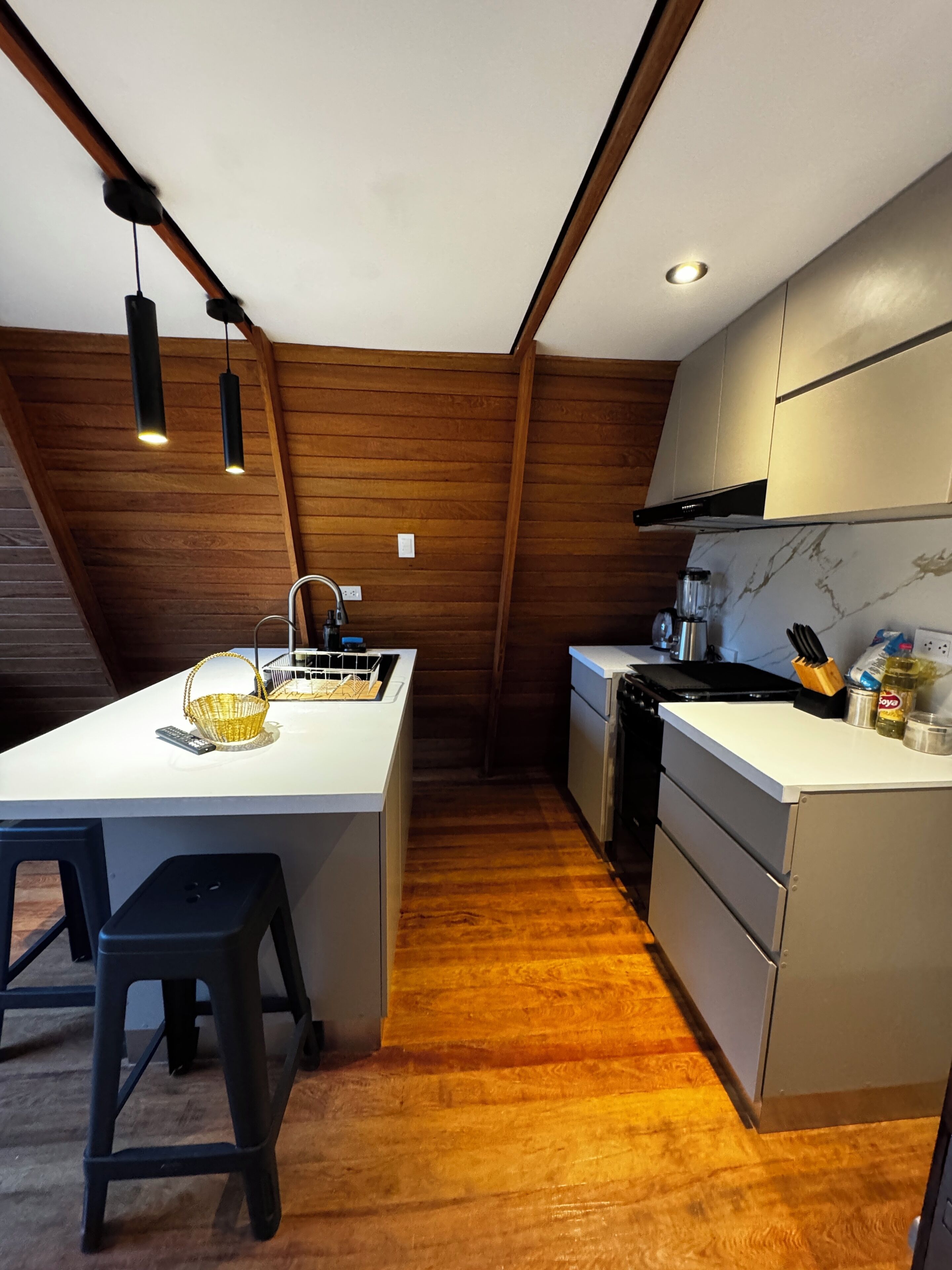 A modern kitchen with wooden walls, a white countertop, and a central island with stools.