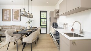 Et moderne køkken med opvaskemaskine, et spiseområde med et bord dækket til fire og et stort vindue med persienner.
