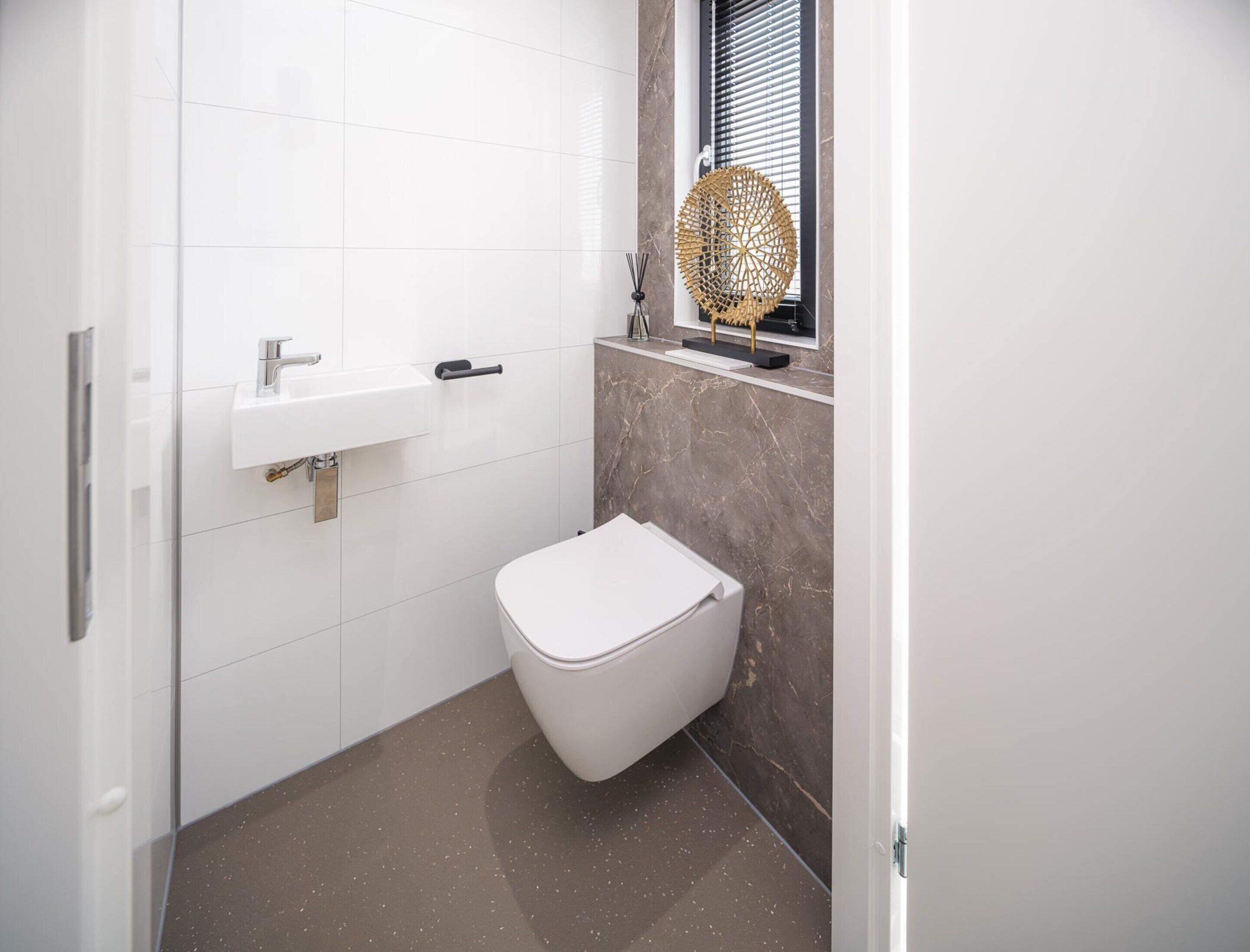 Une salle de bain moderne avec des toilettes blanches, un lavabo et une fenêtre équipée de stores.