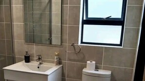 A bathroom with a toilet, sink, mirror, and window. - Luxury 1BR at Blyde Lagoon, Wifi and Security (Pretoria)