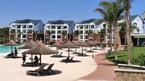 A resort with beachside lounge chairs, thatched umbrellas, and modern buildings with solar panels. - Luxury 1BR at Blyde Lagoon, Wifi and Security (Pretoria)