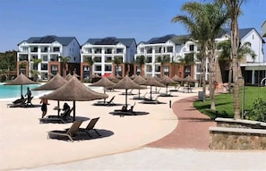 A resort with a pool area, sun loungers, and thatched umbrellas.