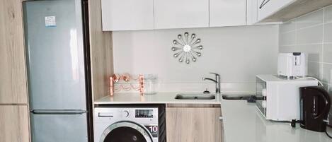 Una cocina compacta equipada con lavadora, refrigerador, cafetera y microondas.
