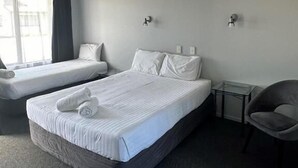 Habitación de hotel con dos camas, una mesita, una silla y un ventanal con cortinas.