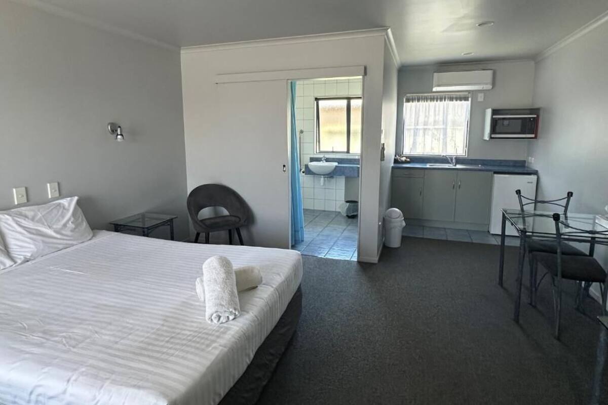A hotel room with a bed, a desk, a chair, a sink, and a window.