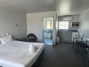 A hotel room with a bed, a desk, a chair, a sink, and a window.