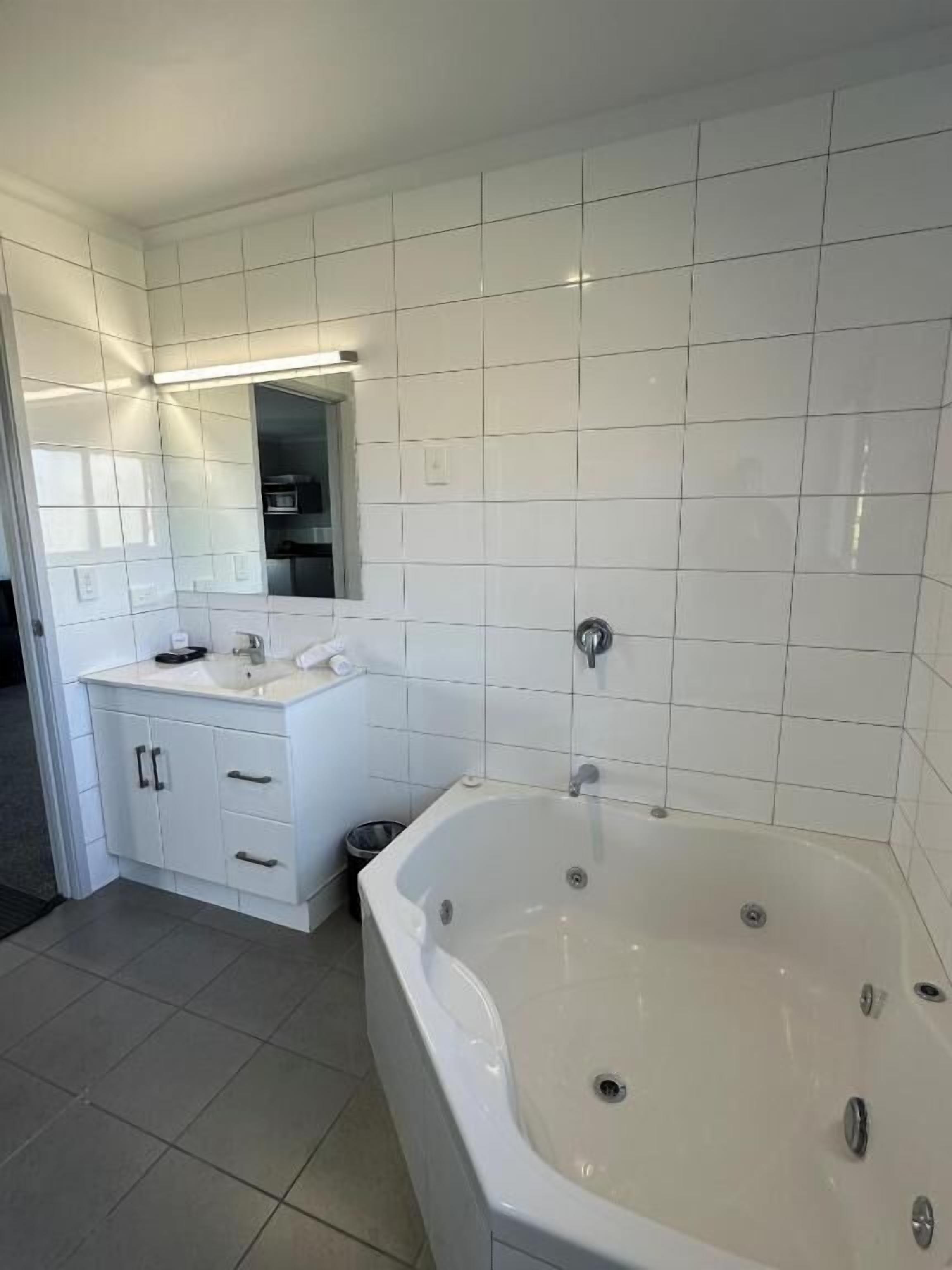 A modern bathroom with white tiles, a large bathtub, a vanity with a mirror, and a sink.
