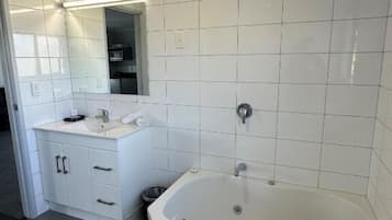 A modern bathroom with white tiles, a large bathtub, a vanity with a mirror, and a sink.