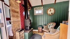 A cozy room with a wood-burning stove, a comfortable chair, a small table, and a mirror on the wall.