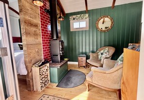 Um quarto aconchegante com uma lareira a lenha, uma poltrona confortável, uma mesinha e um espelho na parede.