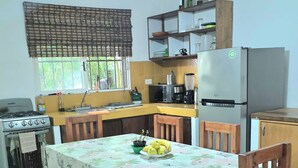 Una cucina con tavolo da pranzo, sedie, una panca, un fornello, un frigorifero e una ventola a soffitto.