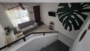 Una scala conduce a una zona living con un divano, una pianta e una TV a parete.