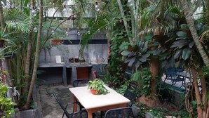 Un patio in cemento con tavolo e sedie, circondato da diverse piante e alberi tropicali.