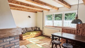 A kitchen with wooden beams, a stone fireplace, a dining area with a table and chairs, and a window with a view of greenery. - Chalet Helena by Interhome (Nové Hamry)