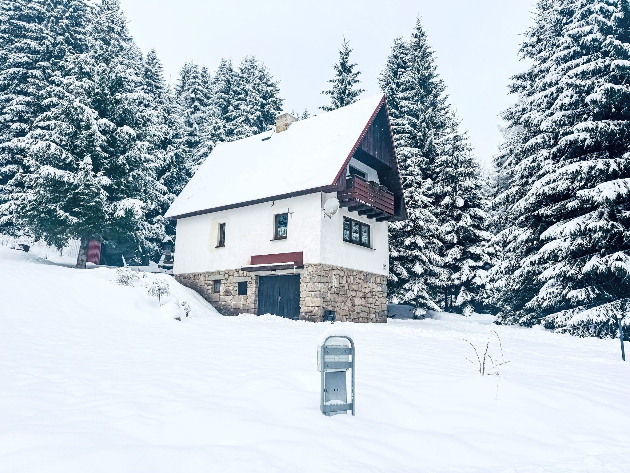 A snow-covered house with a stone foundation, a sloped roof, and a small balcony.
