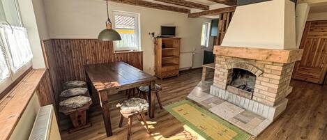 Een rustiek interieur met een houten eettafel, stoelen, een open haard en een groot raam.