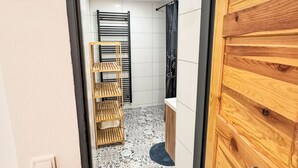 A narrow hallway with a wooden door, a tiled floor, a black metal rack, and a small wooden shelf. - Chalet Helena by Interhome (Nové Hamry)