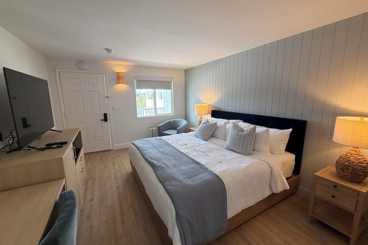 Un dormitorio con cama, mesita de noche, lámpara y televisor sobre un mueble.