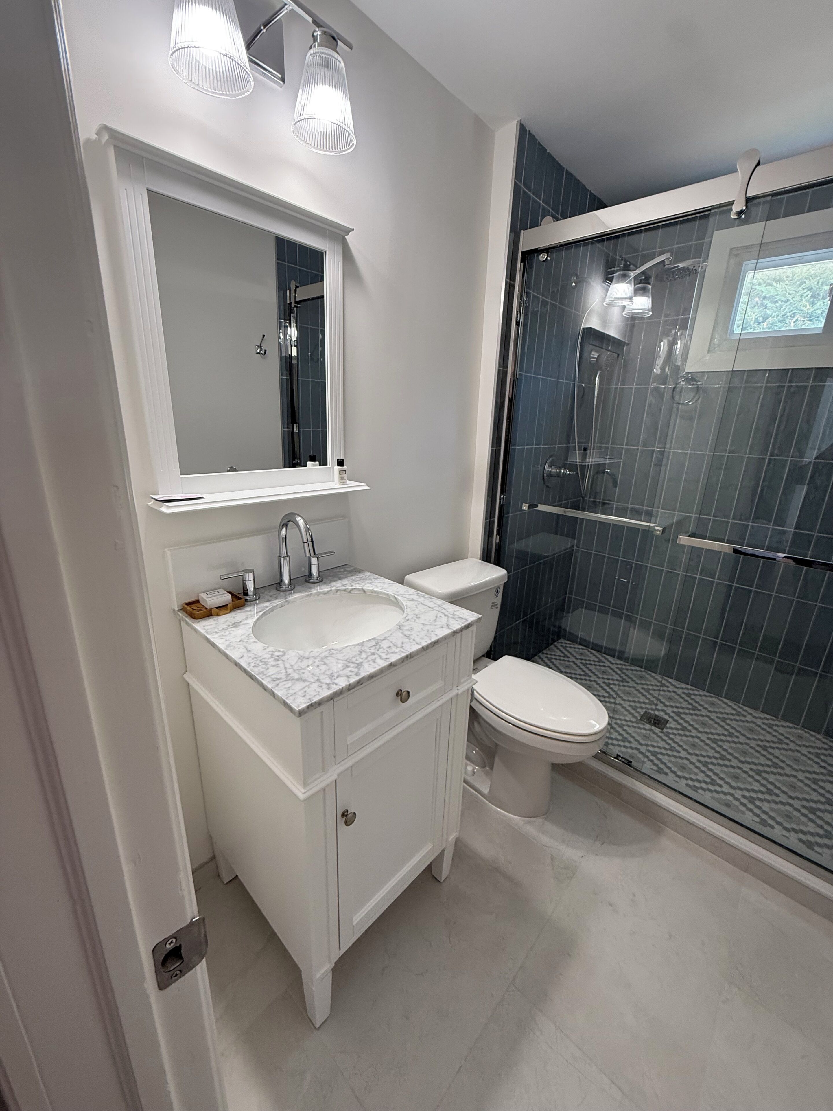 A modern bathroom with a marble sink, a toilet, and a glass-enclosed shower.