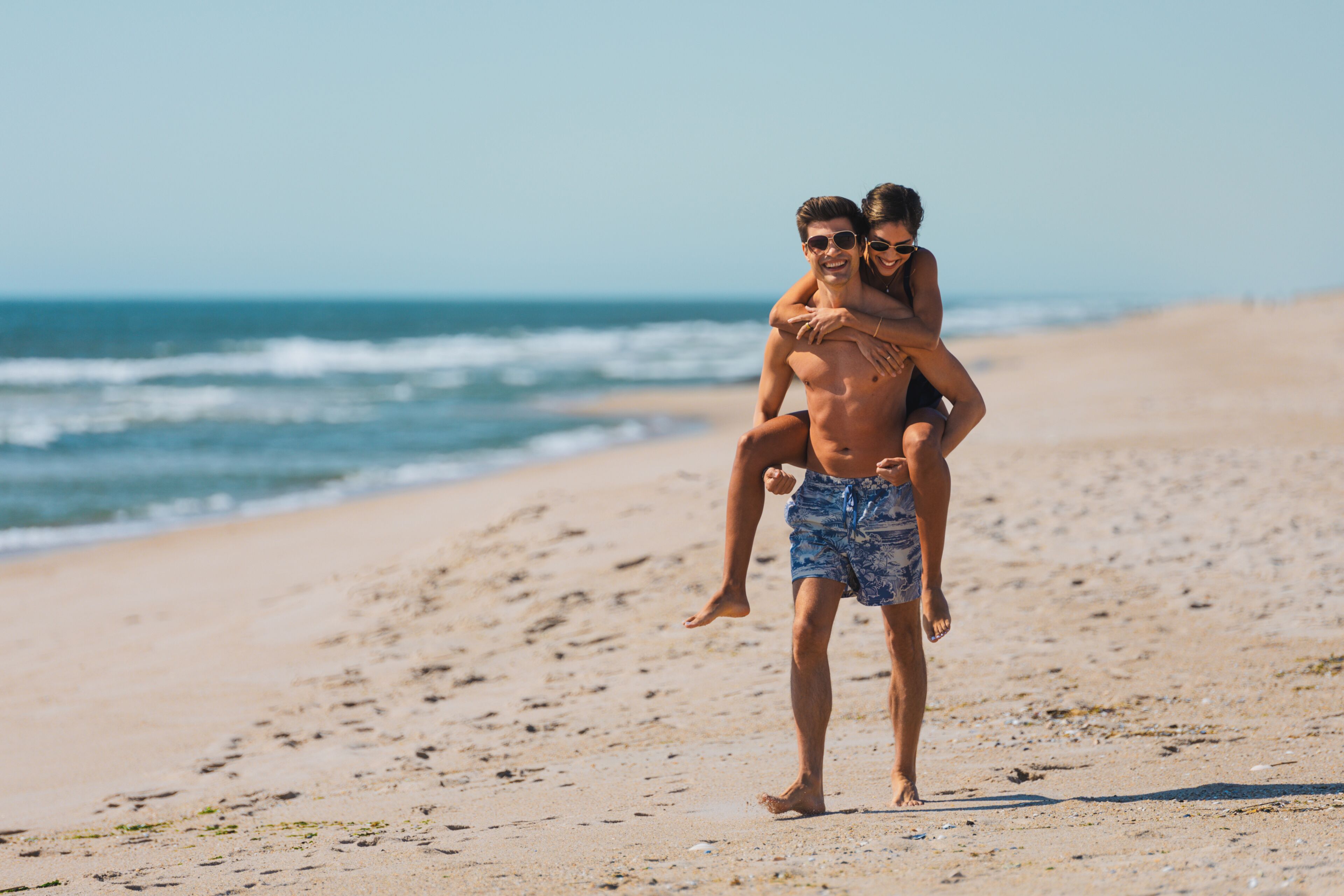 A beach scene with a person carrying another on their shoulders.